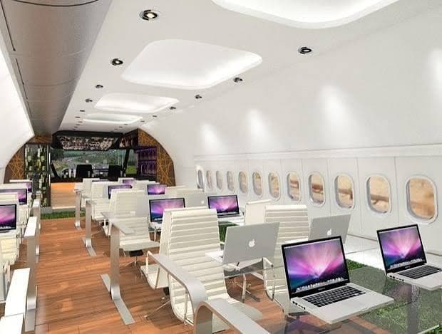 An aircraft cabin converted into an office, with white workstations and laptops along the windows